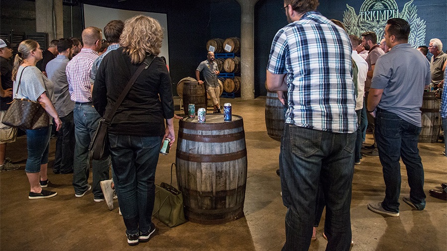 guests besides a barrel in open space listen to a male tour guide 
