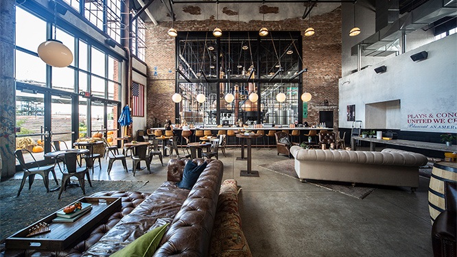 light shines through large glass windows into luxury warehouse taproom with leather seating, exposed brick walls and modern light fixtures