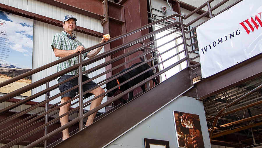 Co-Founder David Defazio, fair skin man in baseball cap and button shirt, stands with his black lab dog on a brown metal staircase 