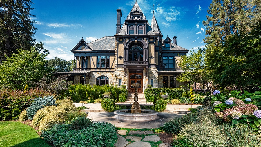 lush green landscaping surrounds the entrance of a beige brick mansion