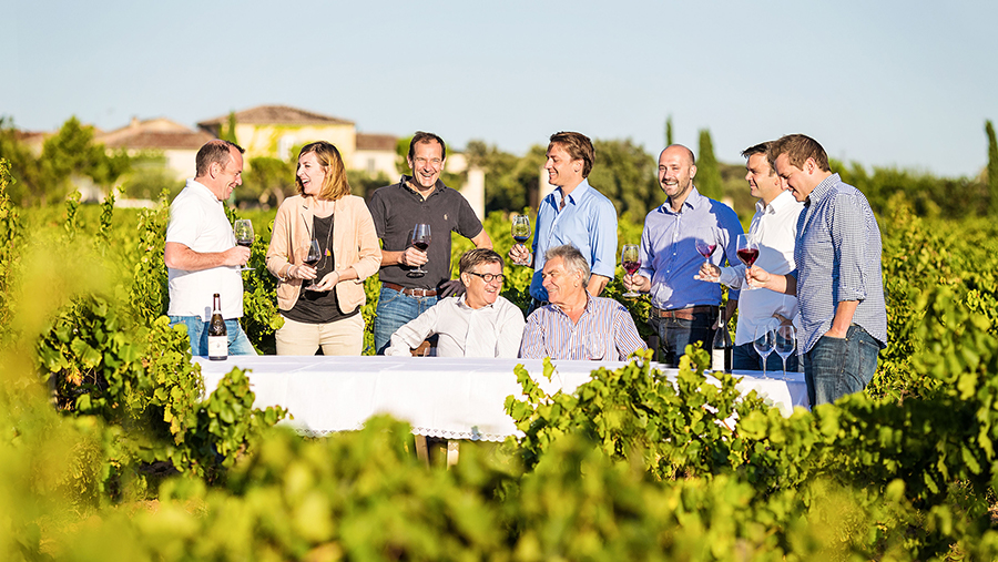 Group of family members drinking red wine gather around for an outdoor table at a vineyard 