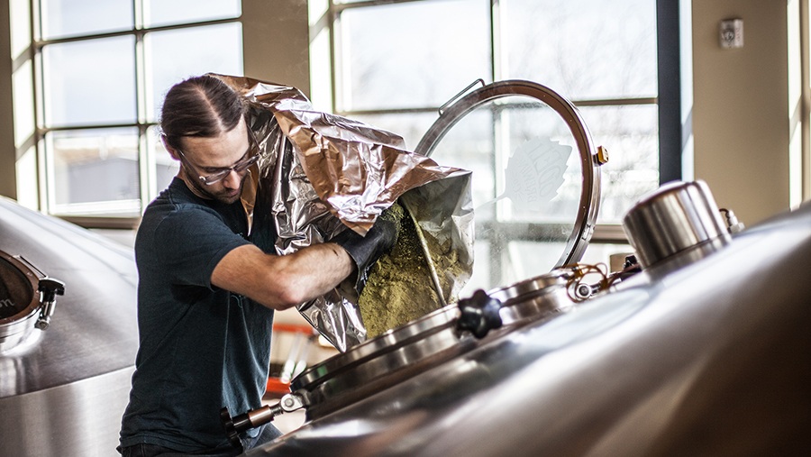 Odell Brewer Jeff Doyle pours hops into a fermentation tank used to brew beer