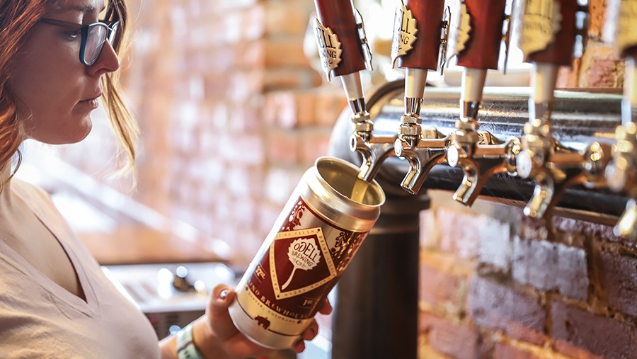 employee at Odell's Rino Taproom pours beer into a crowler from a tap