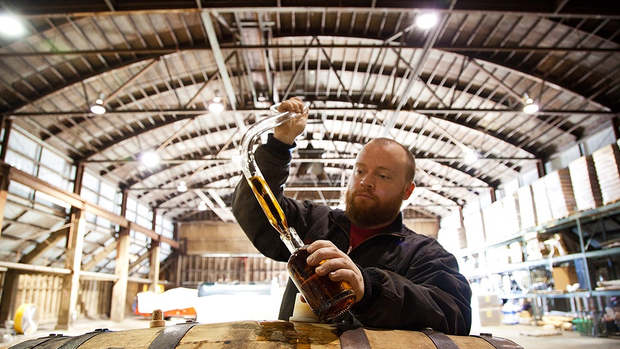 A man extracts whiskey from a cask and transfers it into a glass bottle