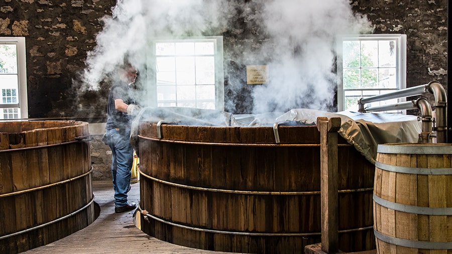 A man stands at a fermentation tank with steam rising up from out of the tank